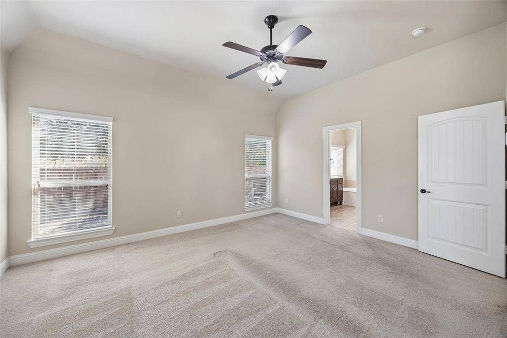 901 Memory Lane, McKinney, TX 75072 Vaulted ceiling with a ceiling fan light fixture, two windows with blinds, a white paneled door, and neutral-toned carpeting