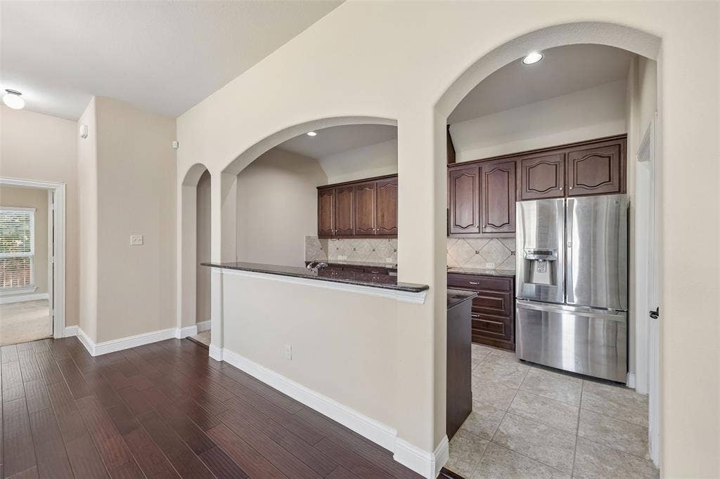 901 Memory Lane, McKinney, TX 75072 Dark wood-finish flooring, arched doorways, a breakfast bar with a dark countertop, stainless steel refrigerator, and dark wood cabinetry