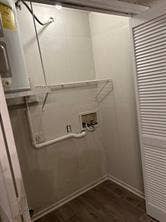 Utility area featuring wood-finish flooring, a water heater, and a bi-fold louvered door