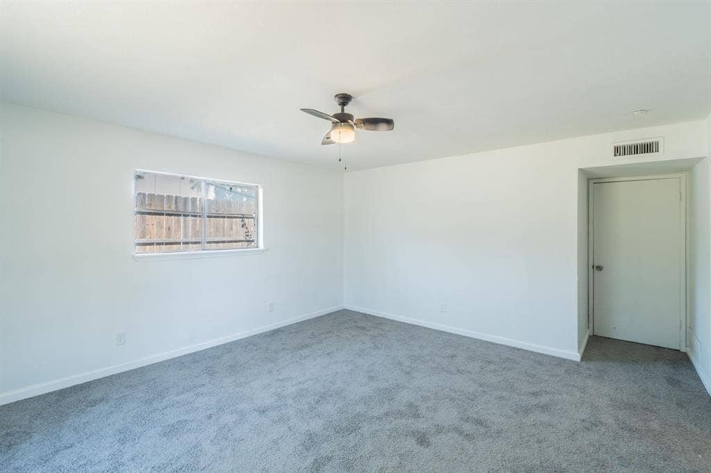 4312 Woodbluff Drive, Mesquite, TX 75150 Light gray carpeting throughout, white painted walls, a window with a security screen, and a ceiling fan with integrated lighting