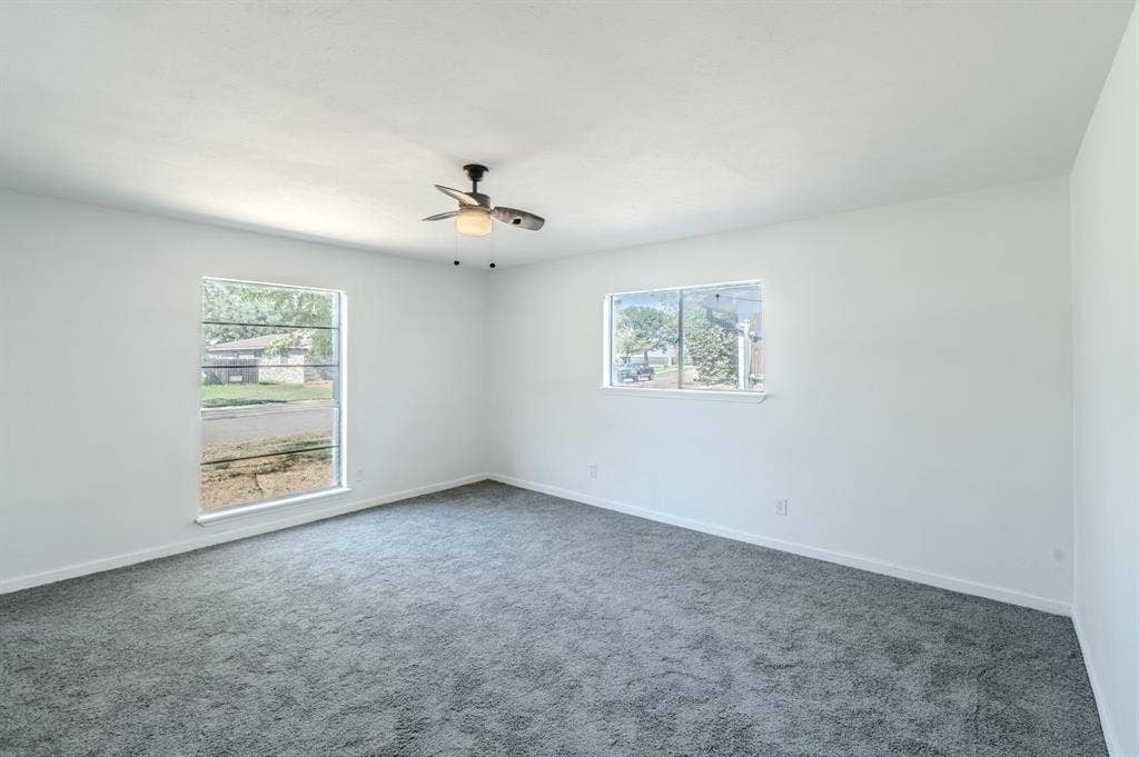 4312 Woodbluff Drive, Mesquite, TX 75150 Bright interior space with light-toned walls, dark gray carpeting, and a ceiling fan with integrated lighting