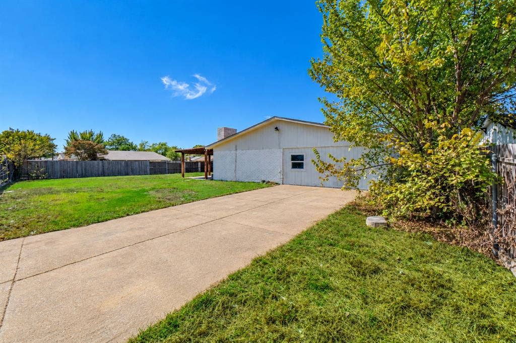4312 Woodbluff Drive, Mesquite, TX 75150 Expansive concrete driveway, attached garage, and a wood-fenced backyard featuring a pergola