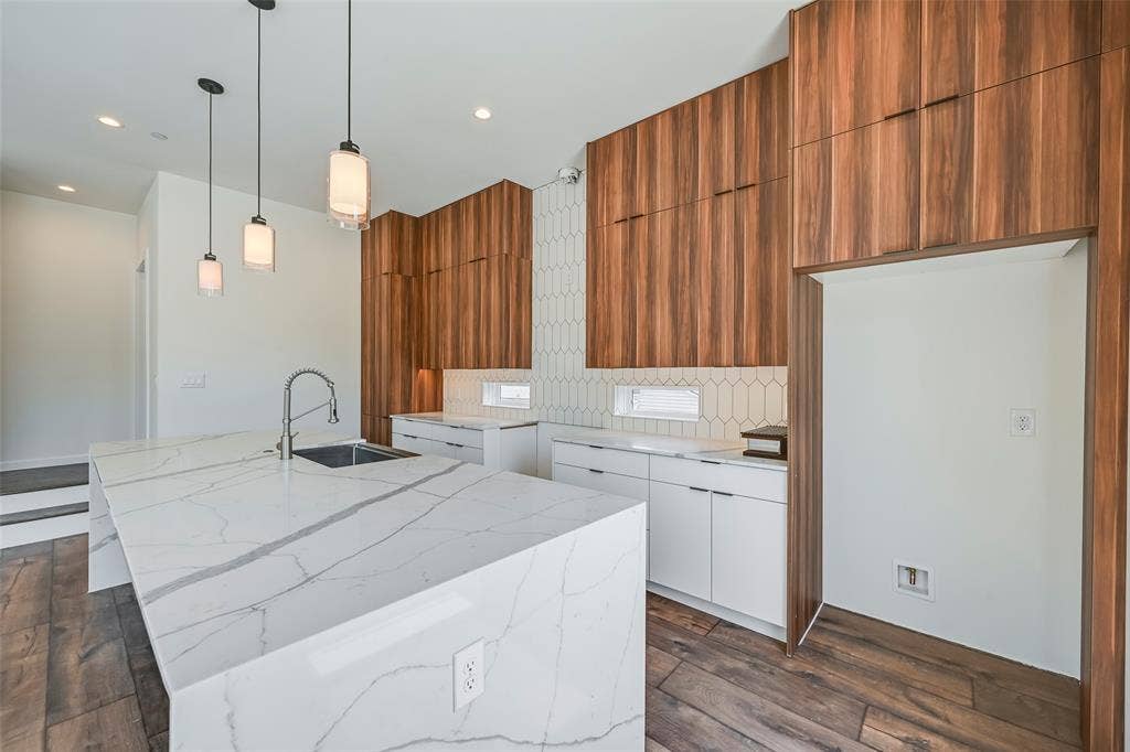 2247 Mail Avenue, #103, Dallas, TX 75235 Kitchen featuring a large waterfall-edge island with an undermount sink and gooseneck faucet, wood-finish flooring, white lower cabinetry, and wood-panel upper cabinetry