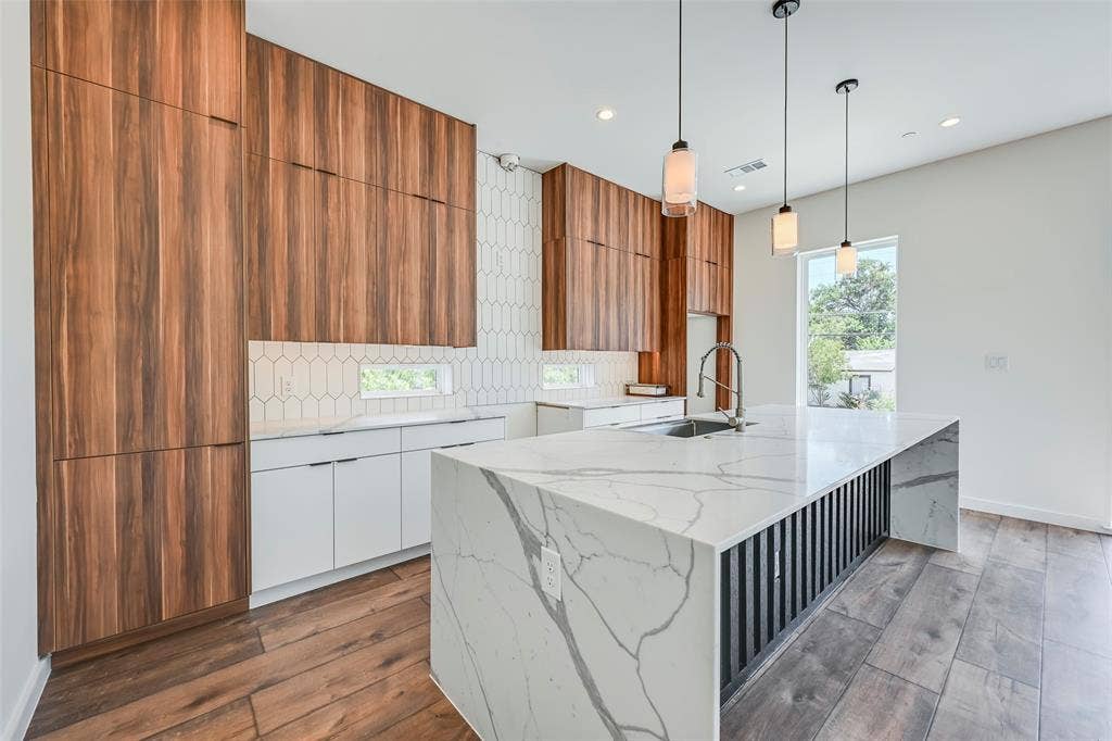 2247 Mail Avenue, #103, Dallas, TX 75235 Kitchen featuring a substantial island with a waterfall counter, wood-finish flooring, full-height wood cabinetry, white shaker-style lower cabinetry, and a geometric tile backsplash