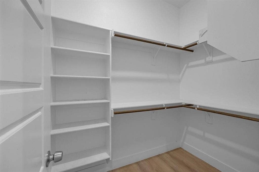 5511 Black Pine Circle, Granbury, TX 76048 Spacious walk-in closet featuring built-in shelving along one wall, dual wooden hanging rods at varying heights, and wood-finish flooring for organized storage and accessibility