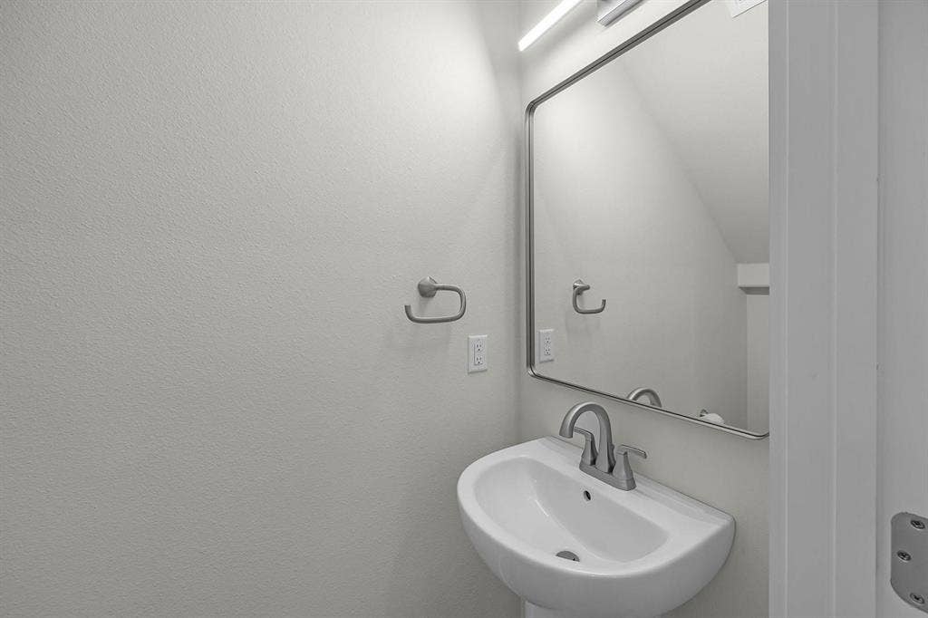 5511 Black Pine Circle, Granbury, TX 76048 Pedestal sink with a polished chrome faucet, framed mirror with integrated lighting, and a coordinating towel ring