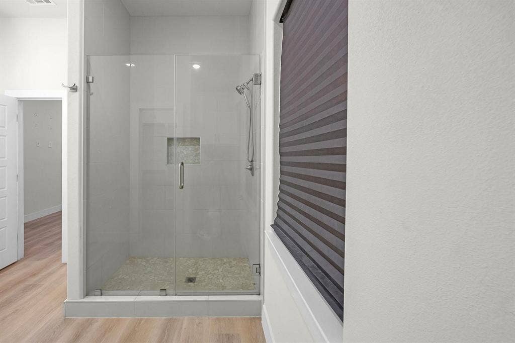 5511 Black Pine Circle, Granbury, TX 76048 Spa-inspired ensuite featuring a frameless glass shower enclosure with brushed nickel hardware, pebble shower floor, and recessed niche shelving