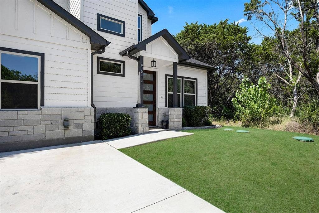 5511 Black Pine Circle, Granbury, TX 76048 Contemporary exterior featuring white siding, a stone facade, an inviting covered entry, and a manicured lawn