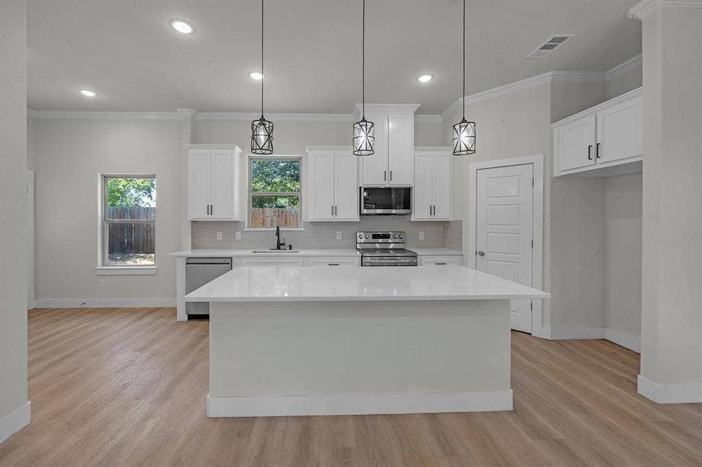 5511 Black Pine Circle, Granbury, TX 76048 Kitchen featuring a large island with white countertops, stainless steel appliances, white cabinetry, and wood-finish flooring