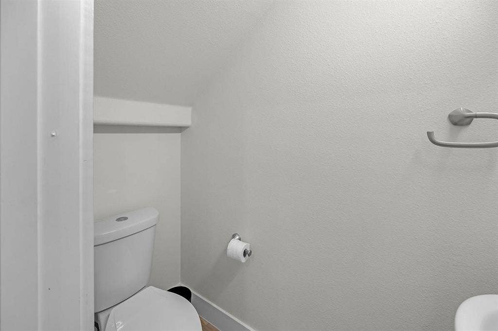 5511 Black Pine Circle, Granbury, TX 76048 White toilet with a built-in shelf, a wall-mounted toilet paper holder, and a metal towel ring