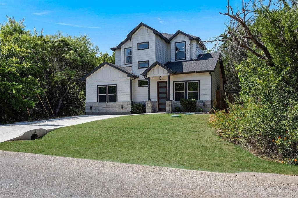 5511 Black Pine Circle, Granbury, TX 76048 Modern farmhouse exterior featuring white siding, black trim windows, a dark wood-finish entry door, and a stone facade