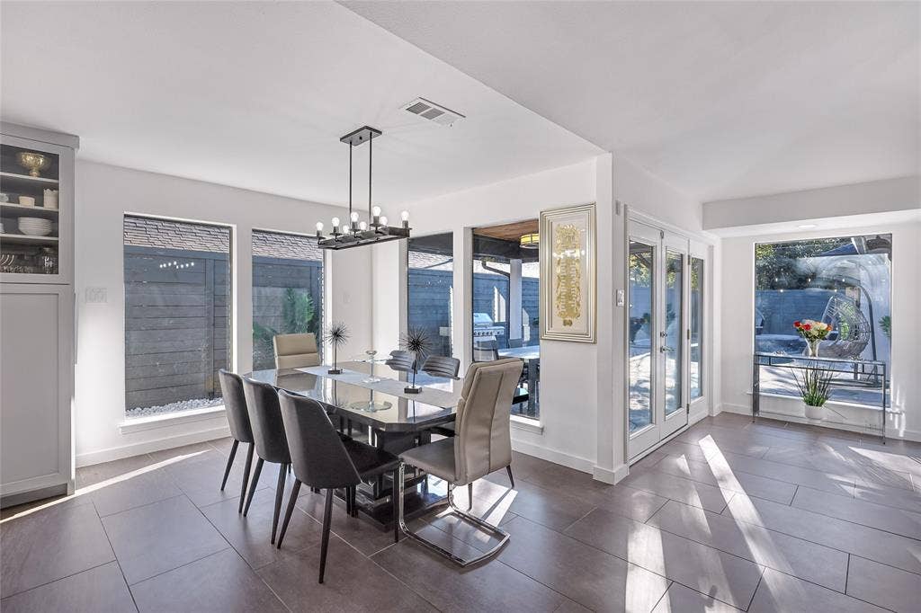 6802 Duffield Drive, Dallas, TX 75248 Modern dining area flooded with natural light through expansive glass doors and windows, featuring a dark wood-finish dining table, contemporary pendant lighting, and sleek dark-finish chairs