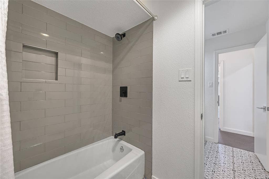 6802 Duffield Drive, Dallas, TX 75248 Bathtub with subway tile surround, recessed shower niche, and matte black fixtures