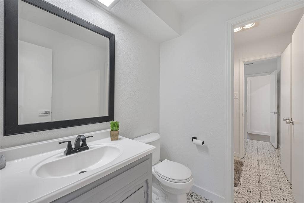 6802 Duffield Drive, Dallas, TX 75248 Bathroom featuring a single vanity with an integrated sink, a dark framed mirror, and a black faucet