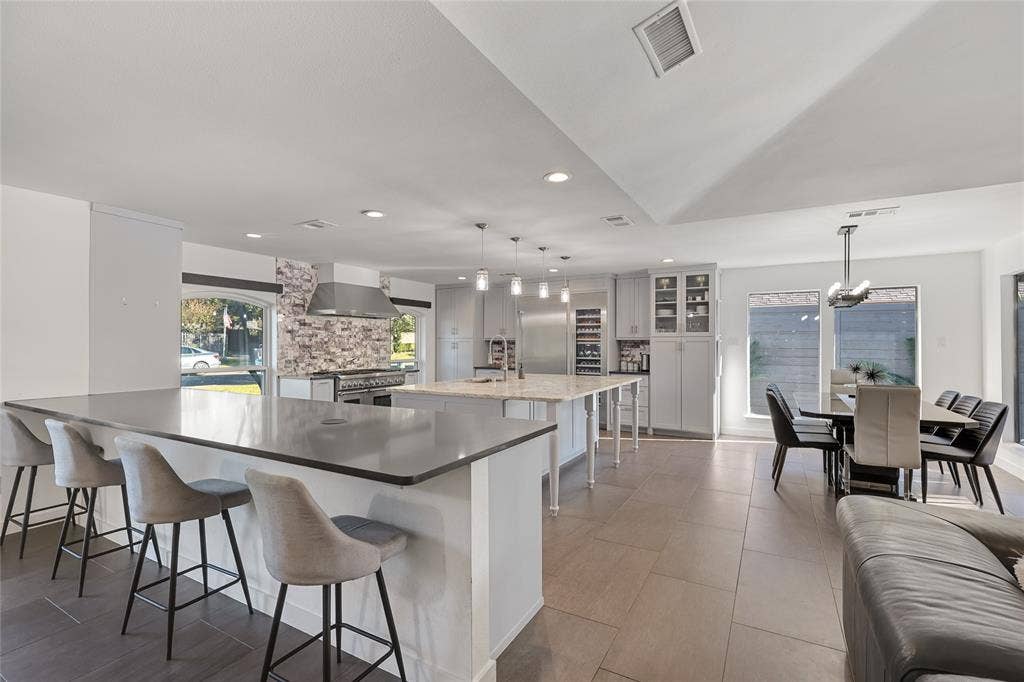 6802 Duffield Drive, Dallas, TX 75248 Spacious open-concept living area featuring an expansive kitchen island with seating, a secondary kitchen island, a dining area, built-in cabinetry, and tile flooring