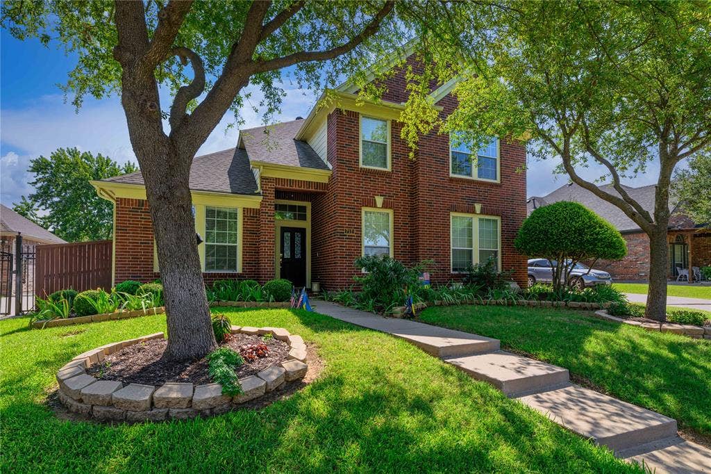 Brick exterior with light-colored trim, concrete walkway, established landscaping, and mature trees