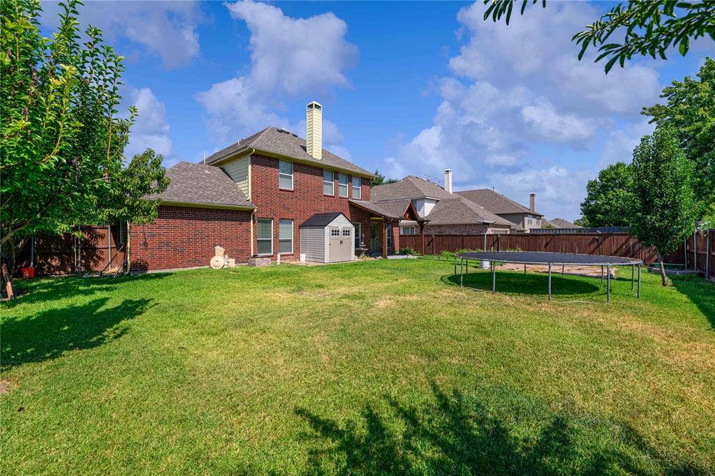Spacious backyard featuring a manicured lawn, brick exterior, wood fence, and mature trees