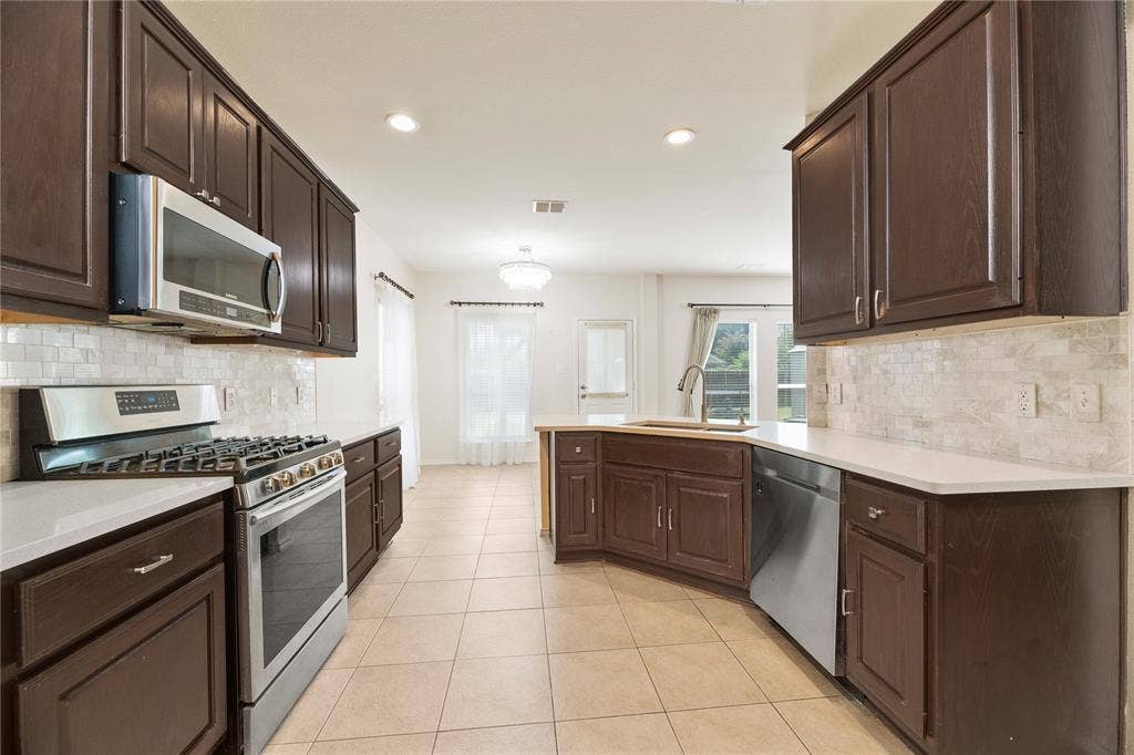Kitchen featuring dark wood cabinetry, stainless steel appliances, light-toned countertops, tile flooring, and a tiled backsplash