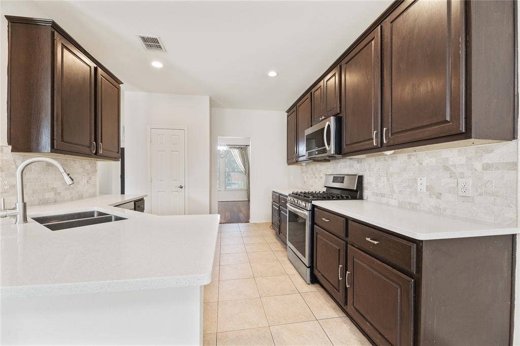 Galley kitchen featuring dark wood cabinetry, light-toned countertops, and a tile backsplash