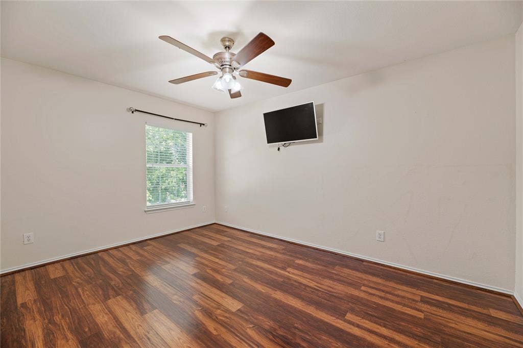Wood-finish flooring, ceiling fan with integrated lighting, single window with blinds, wall-mounted display