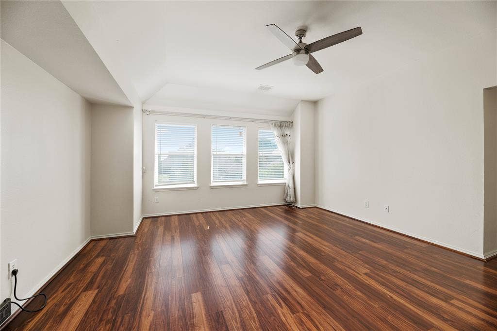 Wood-finish flooring throughout, multiple windows with blinds, and a ceiling fan with integrated lighting