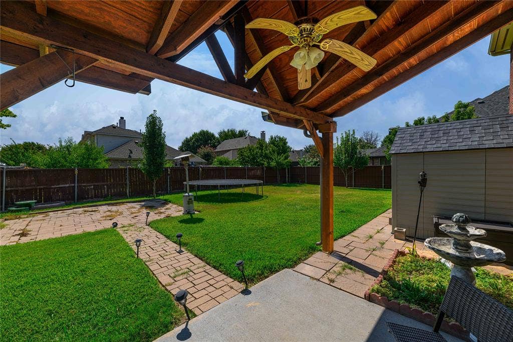 Expansive backyard featuring a covered patio with exposed wood beams and a ceiling fan, a storage shed, and a stone-paver walkway