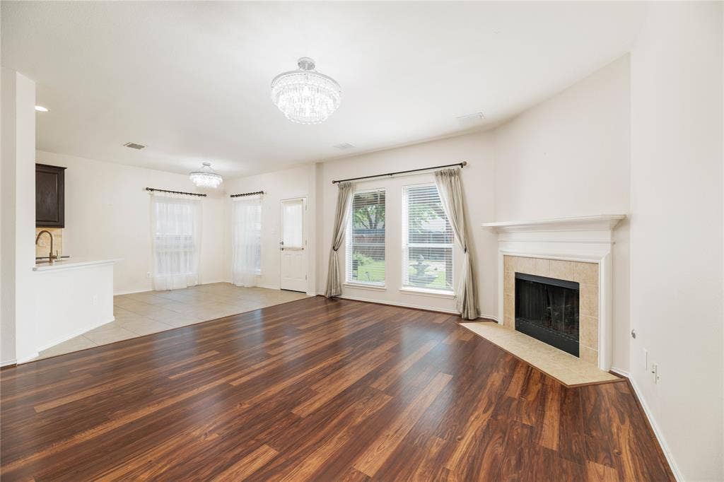 Spacious living area showcasing rich wood-finish flooring, a gas fireplace with surround mantel, recessed lighting, and multiple windows with custom drapery