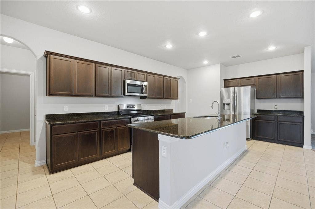 408 Northgate Drive, Terrell, TX 75160 Kitchen featuring dark wood-finish cabinetry, stainless steel appliances, a center island with sink, and tile flooring