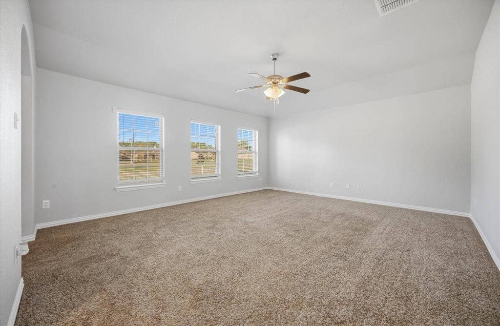 408 Northgate Drive, Terrell, TX 75160 Spacious room featuring neutral carpet flooring, three windows with horizontal blinds, a ceiling fan with integrated lighting, and light-toned wall paint
