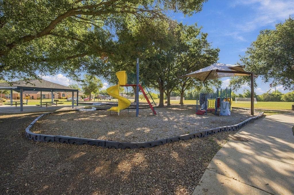 408 Northgate Drive, Terrell, TX 75160 Community park featuring multiple playground structures with slides and climbing equipment, shaded seating areas with umbrellas, mature trees providing natural canopy coverage, and rubber safety surfacing throughout the recreational grounds
