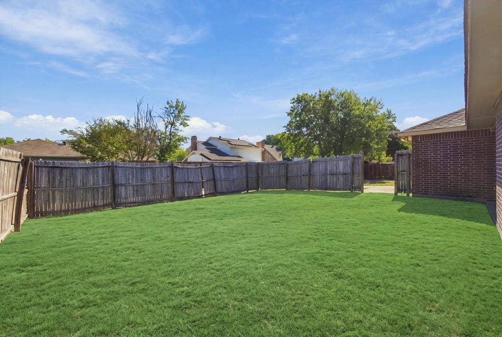 408 Northgate Drive, Terrell, TX 75160 Expansive backyard featuring a meticulously manicured lawn, mature landscaping with established trees, and sturdy wood-finish fencing that provides privacy and definition