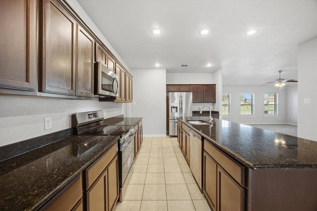 408 Northgate Drive, Terrell, TX 75160 Galley kitchen featuring dark wood cabinetry, a large kitchen island, dark speckled countertops, stainless steel appliances, and tile flooring