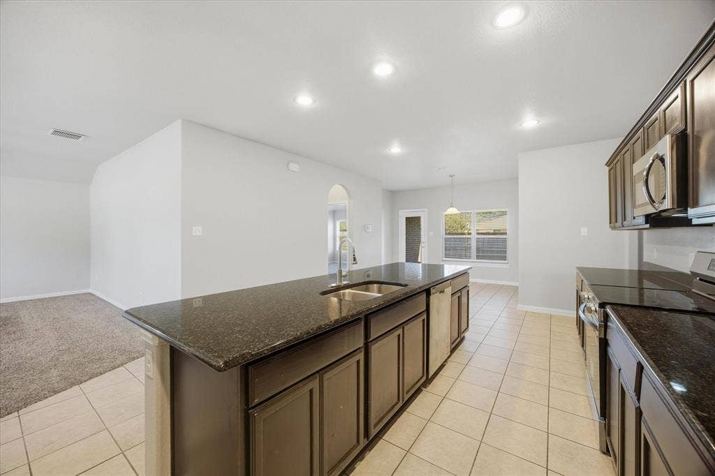 408 Northgate Drive, Terrell, TX 75160 Kitchen featuring dark cabinetry, dark countertops, a stainless steel sink with a high-arc faucet, and integrated stainless steel appliances