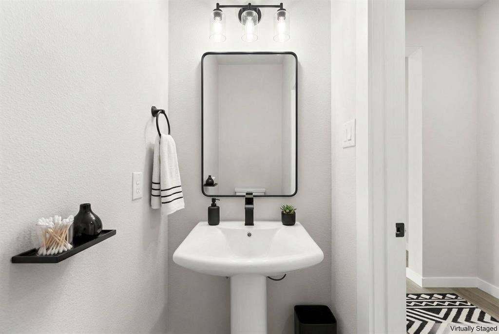 604 Nolan Lane, Wylie, TX 75098 Pedestal sink with a single-handle matte black faucet, rectangular mirror with a matte black frame, and a three-light vanity fixture