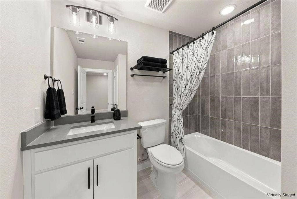 604 Nolan Lane, Wylie, TX 75098 Bathroom featuring a white vanity cabinet with a stone-composite countertop, undermount sink, matte black faucet, and vertical-set grey tile bathtub surround