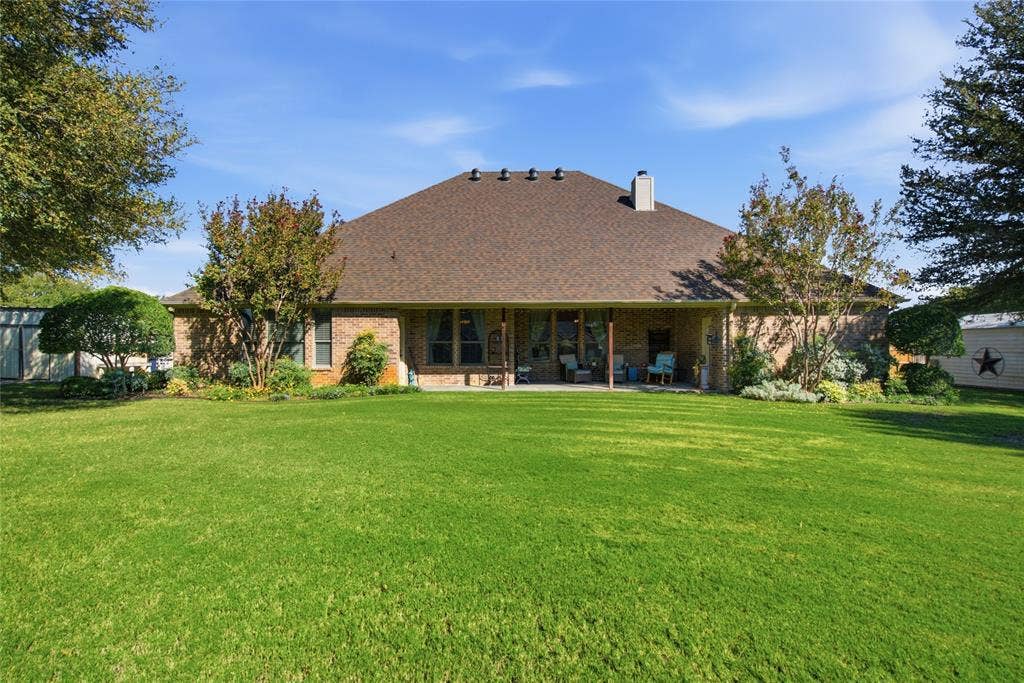Brick exterior residence featuring a hipped roof, covered patio, and expansive lawn with mature landscaping