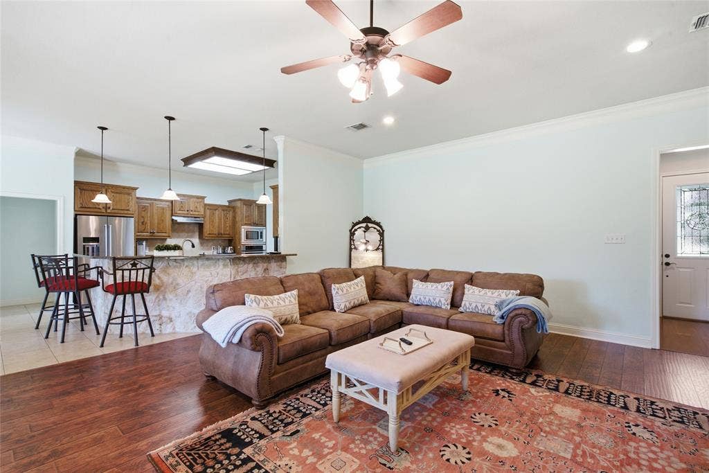 Open concept space featuring wood-finish flooring, a kitchen island with stone cladding, recessed and pendant lighting, and a ceiling fan