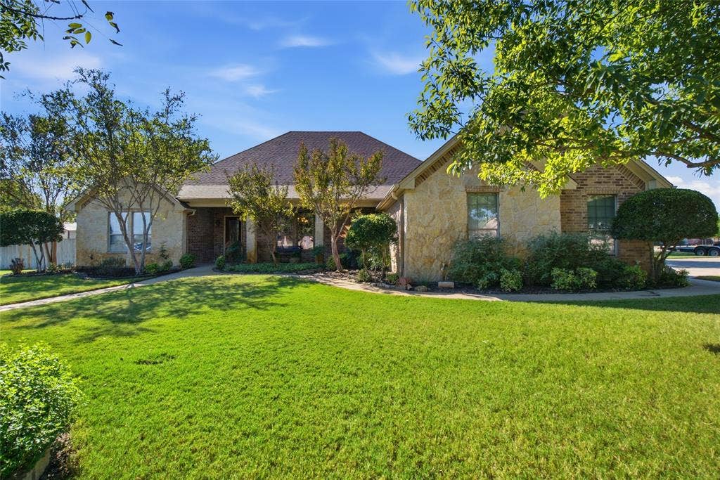 Single-story stone veneer exterior featuring a pitched roof, front-facing gables, expansive lawn, and mature trees