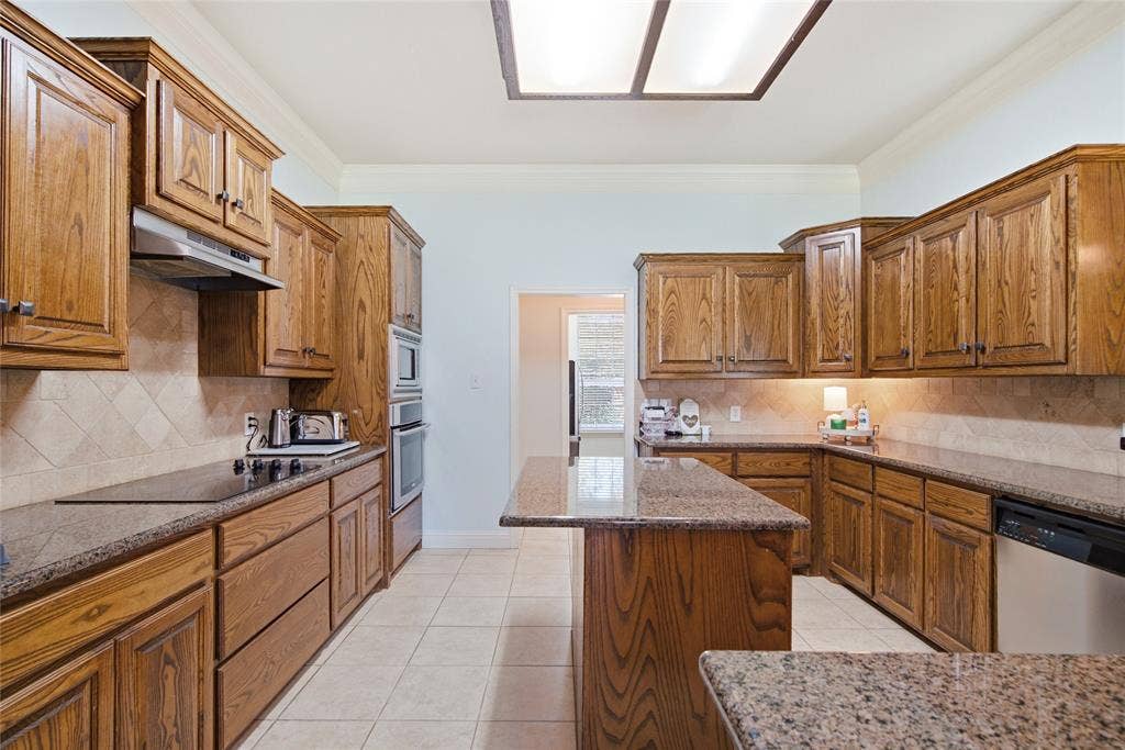 Kitchen featuring wood cabinetry, stone countertops, a central island, tile backsplash, and built-in appliances