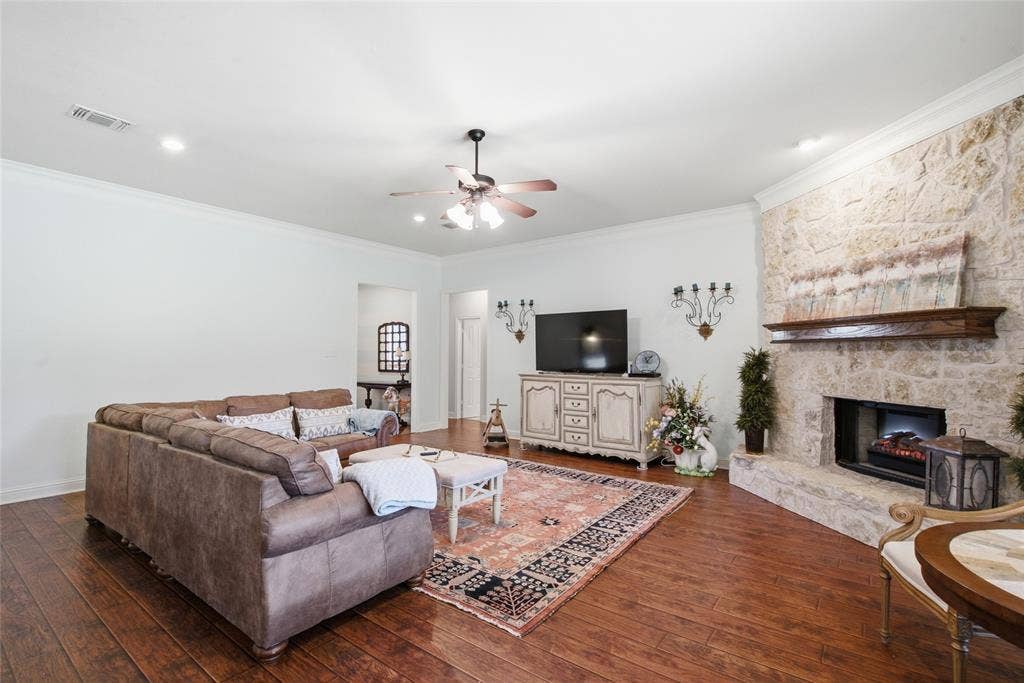 Floor-to-ceiling stone fireplace with a prominent wooden mantel, wood-finish flooring, recessed lighting, and a multi-blade ceiling fan