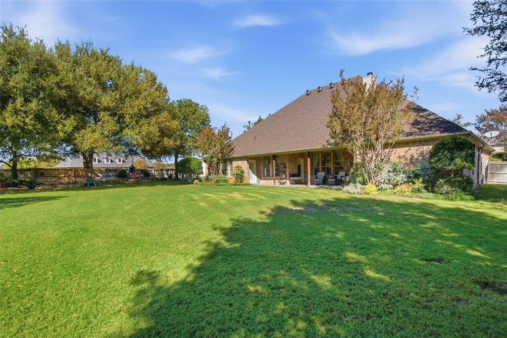 Expansive backyard featuring a large grass lawn, mature trees, and a covered patio area with a brick exterior