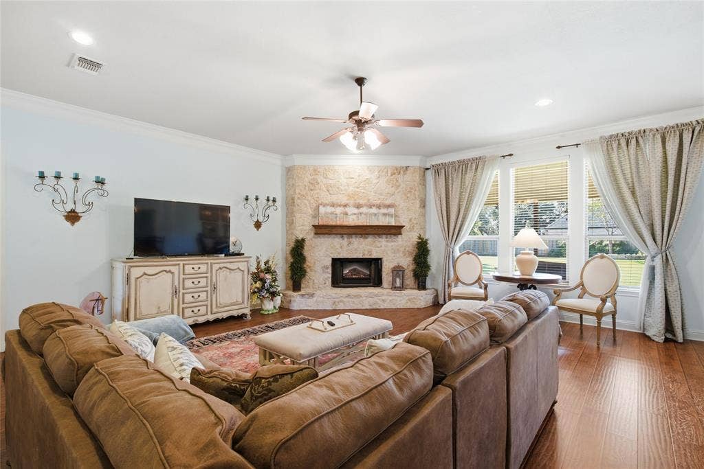 Living area featuring wood-finish flooring, a floor-to-ceiling stone-surround corner fireplace with a wooden mantel, and crown molding