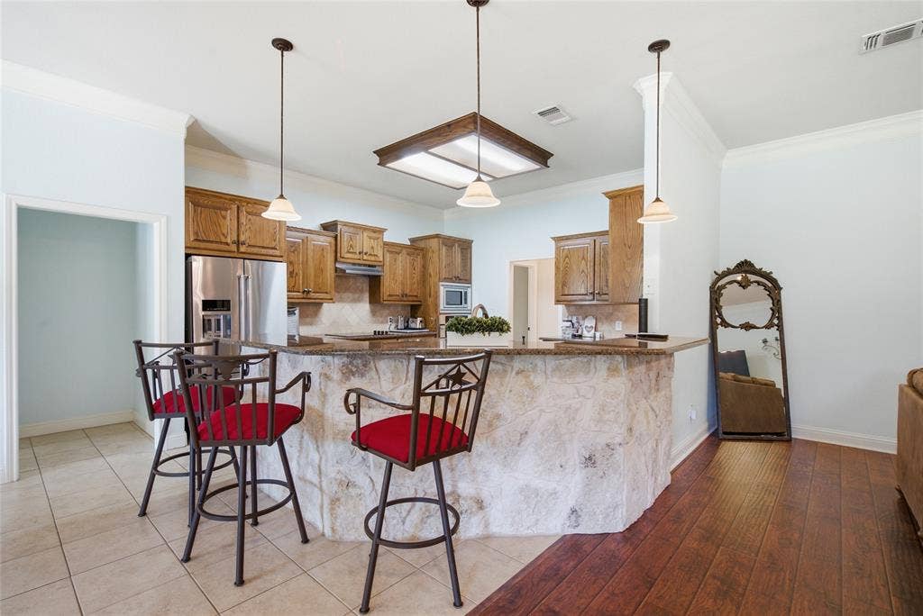 Kitchen featuring stone-front breakfast bar, wood cabinetry, stainless steel refrigerator, recessed lighting with wood-trim fixture, and pendant lighting