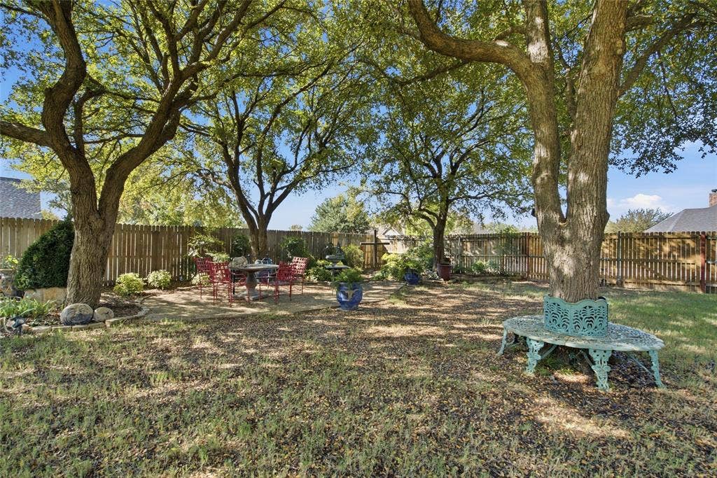 Backyard featuring mature trees, a stone patio, and perimeter wood fencing