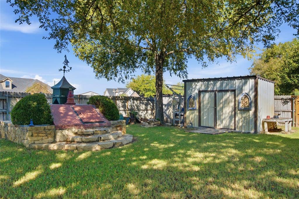 Backyard featuring a custom stone-encased cellar, detached metal storage structure, mature canopy tree, and wood privacy fencing