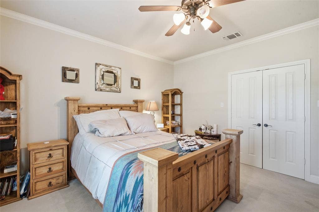 Room featuring tile flooring, ceiling fan with integrated light fixture, crown molding, and wooden wall-mounted cabinetry