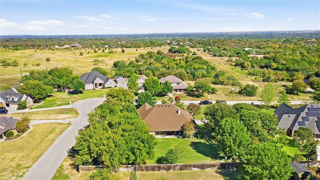 Aerial perspective of a multi-gabled residence featuring a sprawling lawn, mature landscaping, and perimeter wood fencing