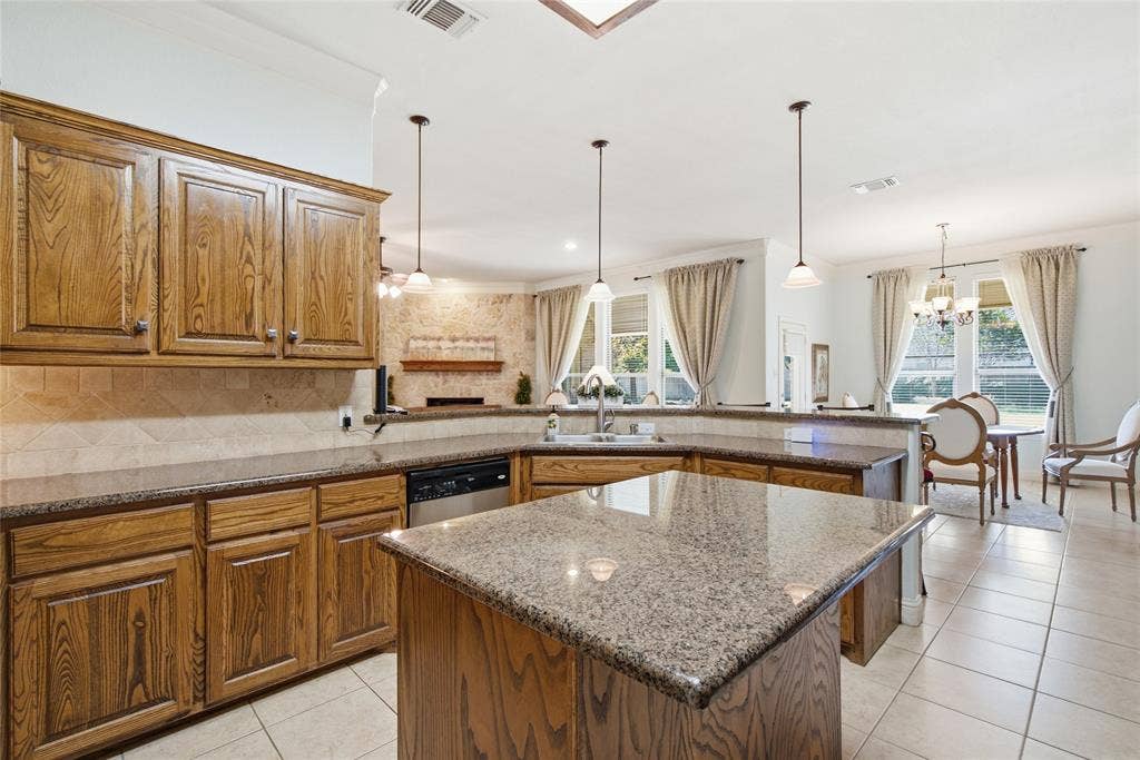 Kitchen featuring stained wood cabinetry, stone-surface countertops, tile backsplash, center island with a built-in sink, and pendant lighting