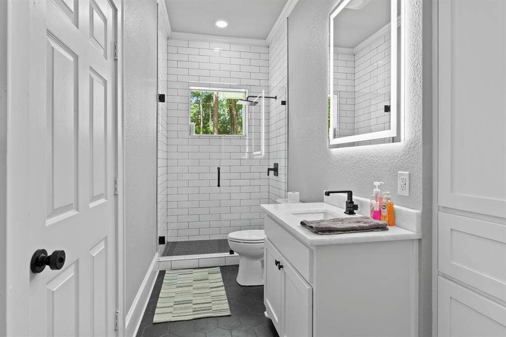 18630 Eastside Road, Troup, TX 75789 Bathroom featuring a white subway tile shower, frameless glass shower enclosure, black hexagon floor tile, and a vanity with a rectangular sink