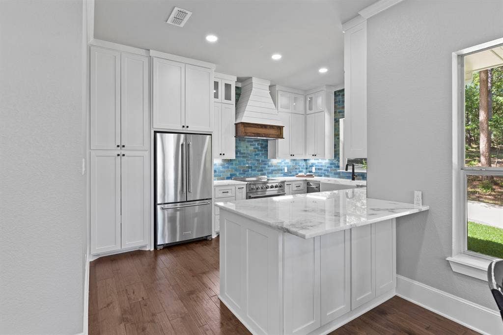 18630 Eastside Road, Troup, TX 75789 Kitchen featuring white cabinetry, stainless steel appliances, a marble-finish island, wood-finish flooring, and a blue tile backsplash
